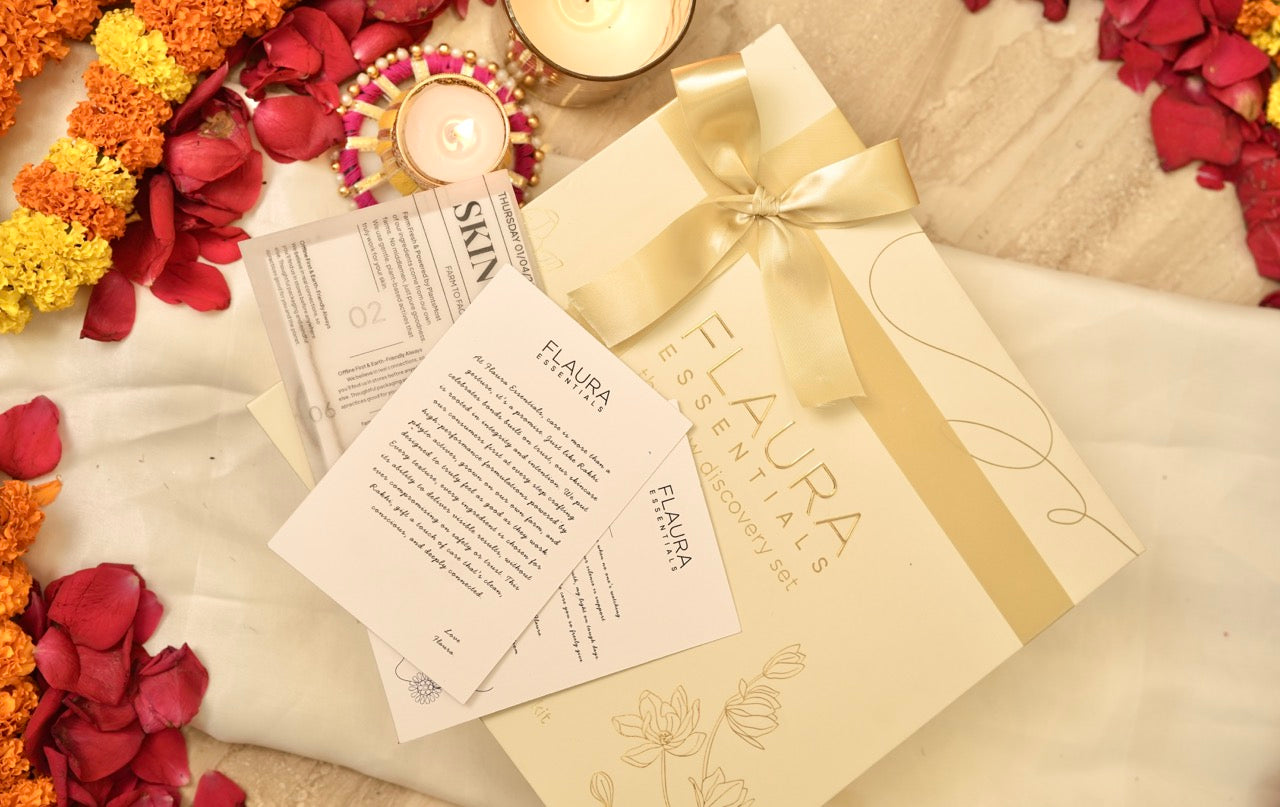 Glow discovery set Gift box with a gold ribbon surrounded by flowers and a card on a textured surface.